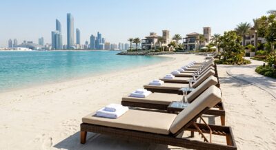 Luxury beachfront resort in Abu Dhabi with folded pool towels on loungers by the water, bright daytime coastal photography, no people or text