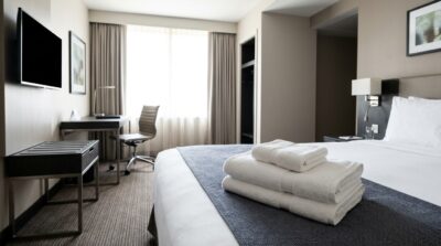 Clean, professional business hotel room with neatly folded white bath towels on the bed, modern minimal styling, daylight through window, no text or logos